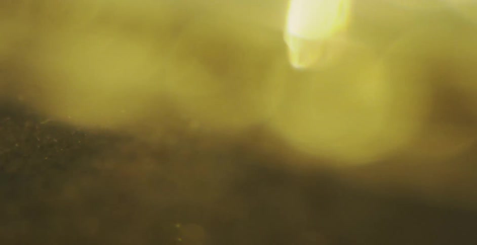 Abstract macro footage shows dark sand and shimmering gold particles moving slowly through a hazy liquid