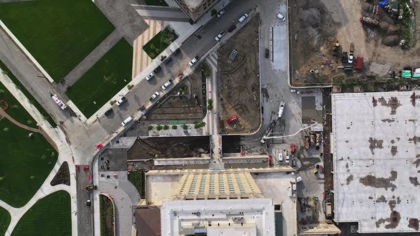 An aerial top-down timelapse of a bustling urban construction site where workers and machinery pour concrete next to a city street and park