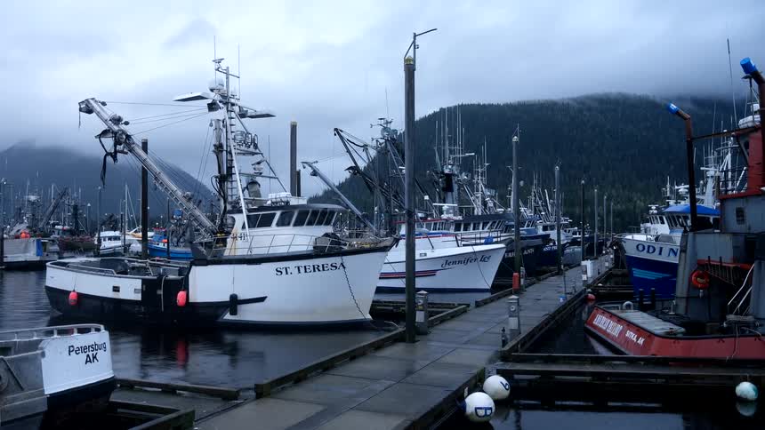 Commercial fishing boats are docked at the pier in an Alaskan harbor on a cloudy and foggy day