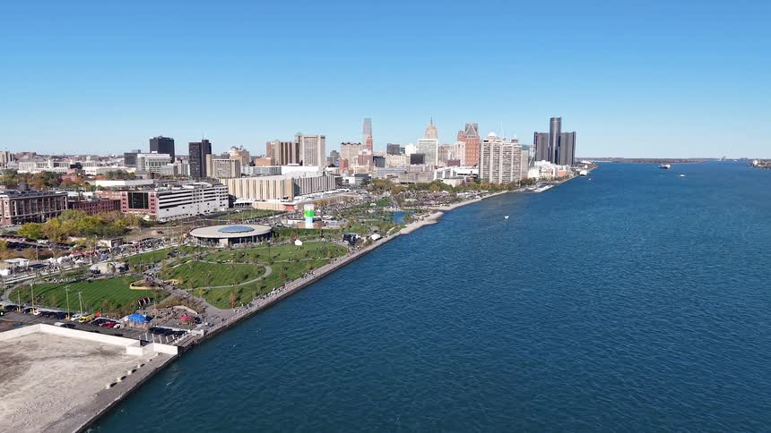Sweeping aerial view of the Detroit, Michigan skyline and waterfront park along the Detroit River on a clear, sunny day