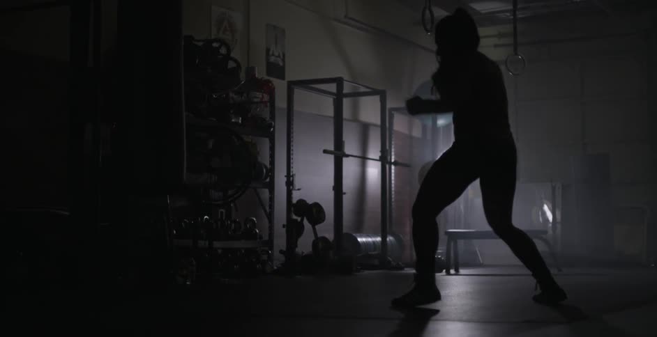 Woman practices boxing moves in a dimly lit gym