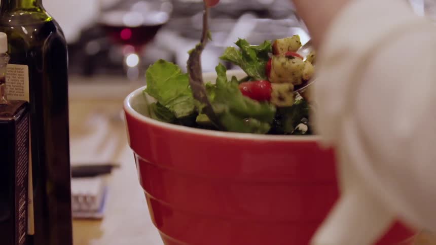 A woman is tossing a salad in a bowl
