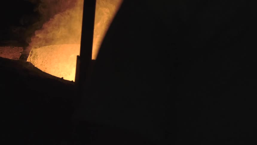 Glowing molten metal steams and bubbles in a large industrial crucible within a dark foundry