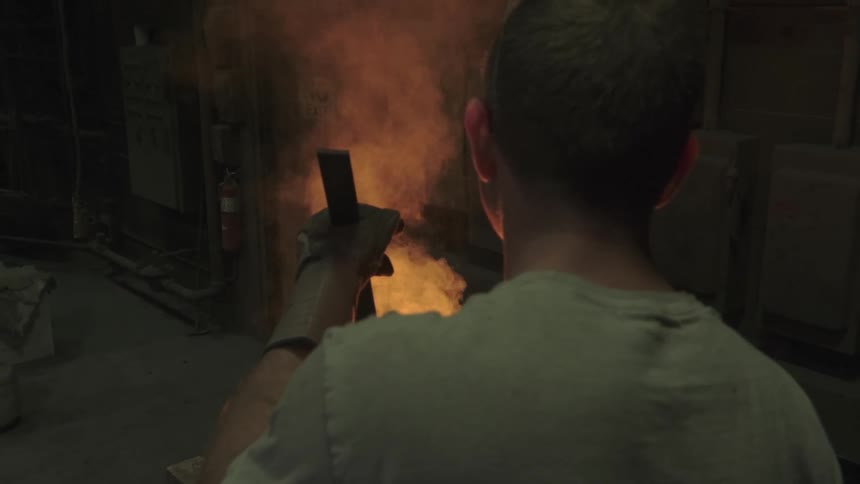Slow motion over-the-shoulder shot of a foundry worker stirring a glowing crucible of molten metal