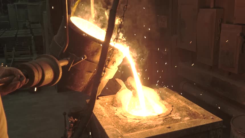 Over the shoulder shot of a factory worker pouring molten liquid into a mold in slow motion