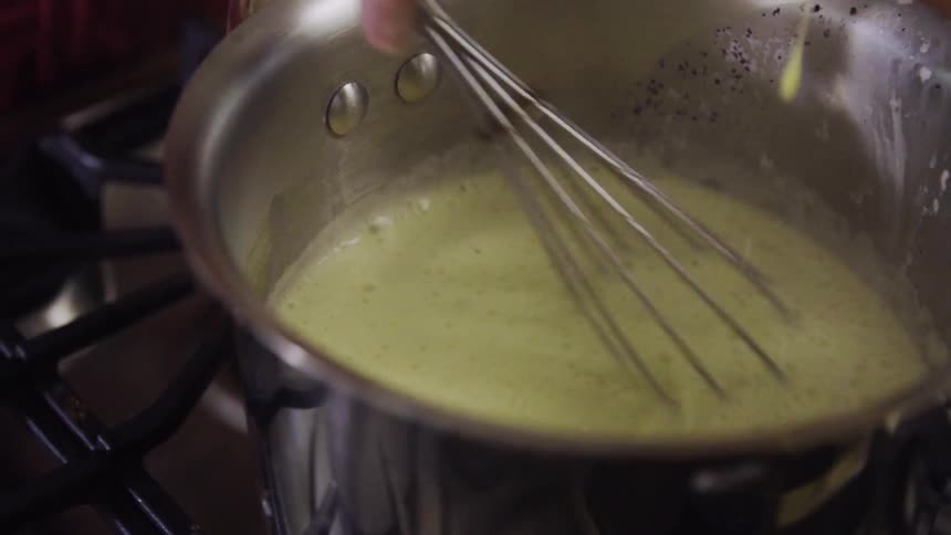 A woman uses a whisk to stir a sauce as it cooks