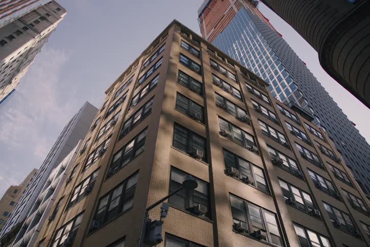 A slow dolly back reveals a street corner amidst towering old and new skyscrapers in a bustling city on a sunny day