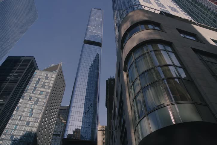A slow dolly shot reveals the towering modern skyscrapers of New York City from a low angle on a sunny day