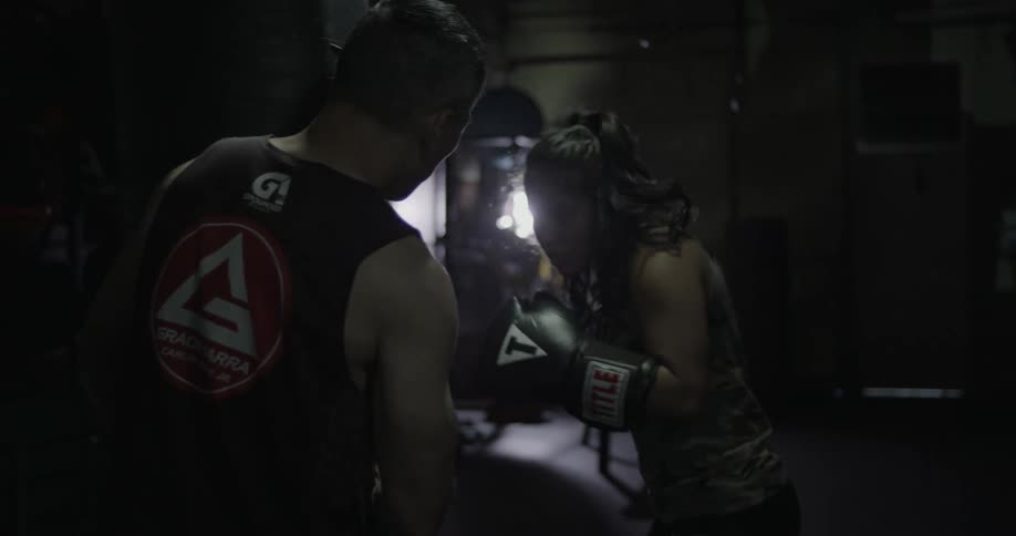 Woman boxing with a trainer in a dark area