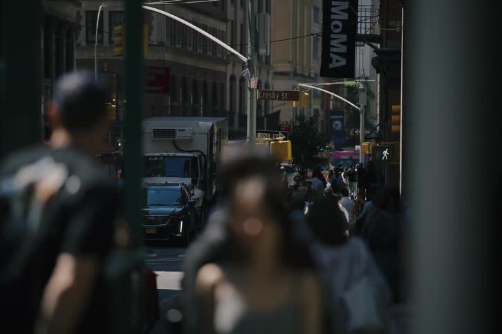 A view of anonymous crowds walking down a sunny Crosby Street in SoHo, New York City, with blurred pedestrians passing in the foreground