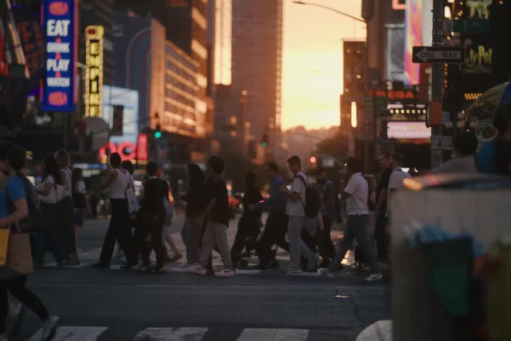 Slow-motion shot of an anonymous crowd of pedestrians crossing a busy New York City street during a vibrant sunset