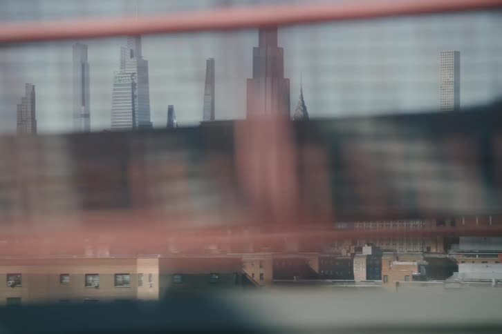 A gritty, handheld perspective of the New York City skyline as seen from a moving elevated subway car