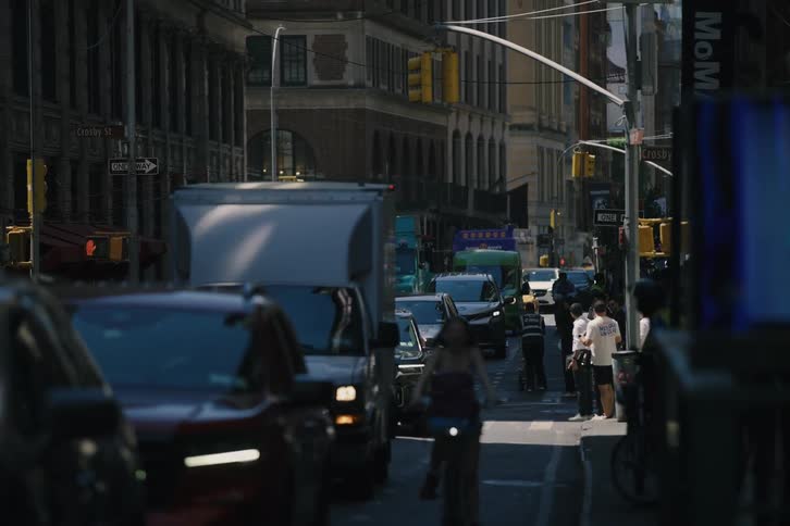 Slow-motion telephoto shot of a woman riding a bicycle through a busy city street in New York