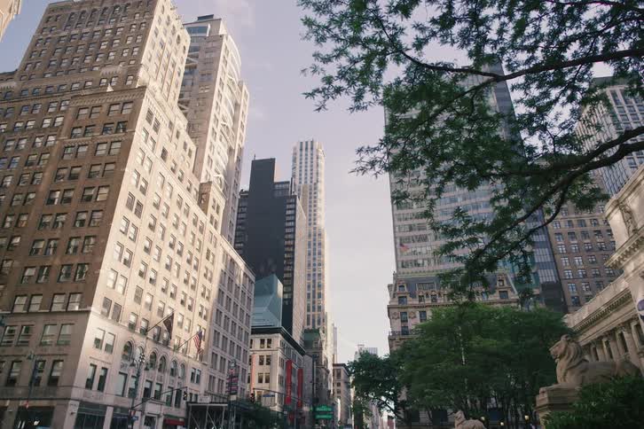 A slow zoom out from the towering skyscrapers on 5th Avenue next to the New York Public Library on a sunny day