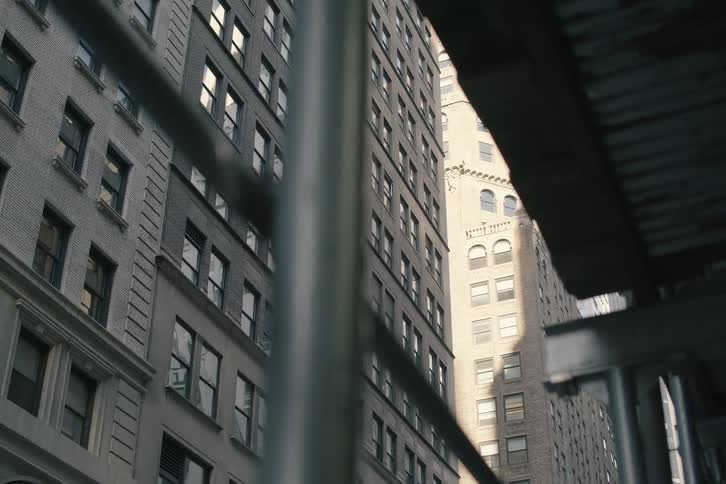 A slow dolly shot reveals classic city apartment buildings from underneath the dark metal structure of sidewalk scaffolding