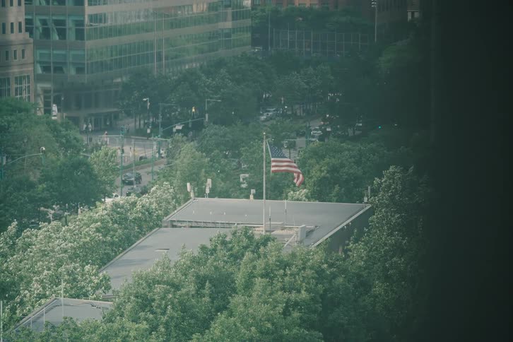 An American flag waves proudly atop a building surrounded by lush green trees in a bustling city