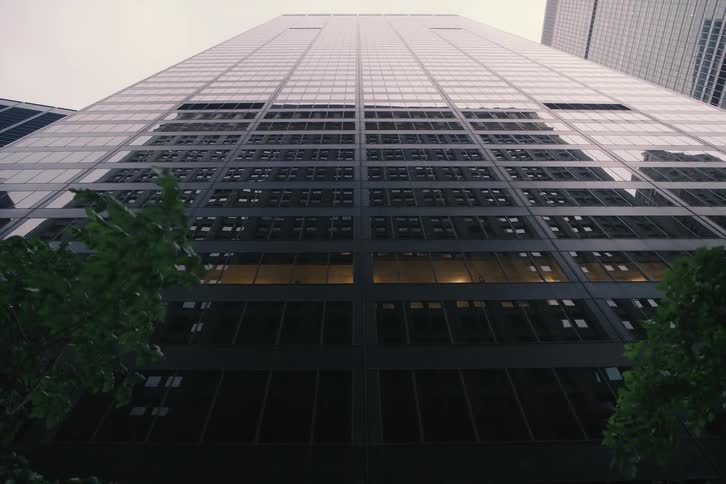 A slow, low-angle dolly out from a towering glass and steel skyscraper in a modern city