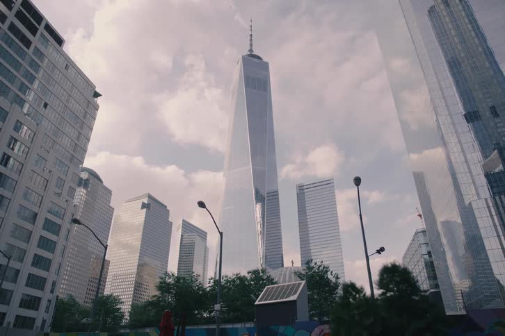 A low-angle, slow pull-back shot of the One World Trade Center and surrounding skyscrapers in Manhattan on a cloudy day