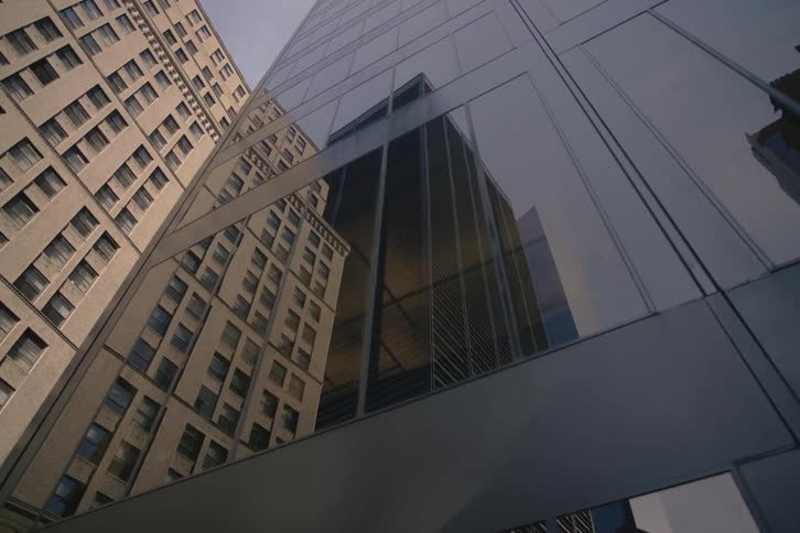 A slow upward pan from the reflective windows of a modern skyscraper reveals the classic architecture of a dense downtown cityscape