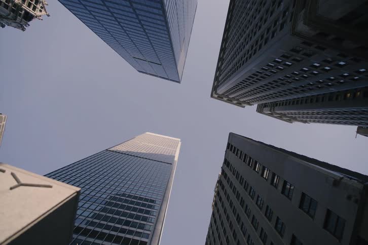 A slow pull-back from a dramatic low-angle shot looking up at four towering skyscrapers against a clear sky