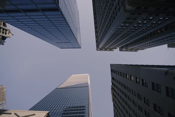 A slow camera pulls back from a low-angle shot of towering city skyscrapers against a clear sky