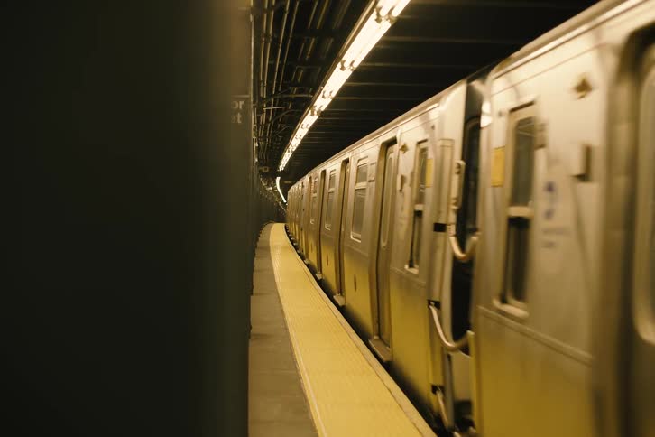 A side view of a New York City subway train as it departs from the Rector Street station, disappearing into the dark tunnel