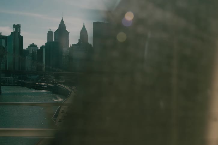 Cinematic tracking shot of the sun-drenched Lower Manhattan skyline as seen from a moving train crossing a bridge