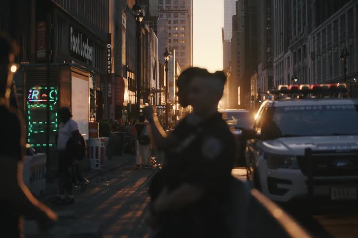 Two female police officers are silhouetted by the setting sun while standing guard on a busy New York City street
