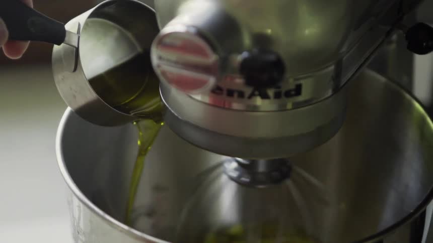 Oil is being poured into the bowl of a working stand mixer