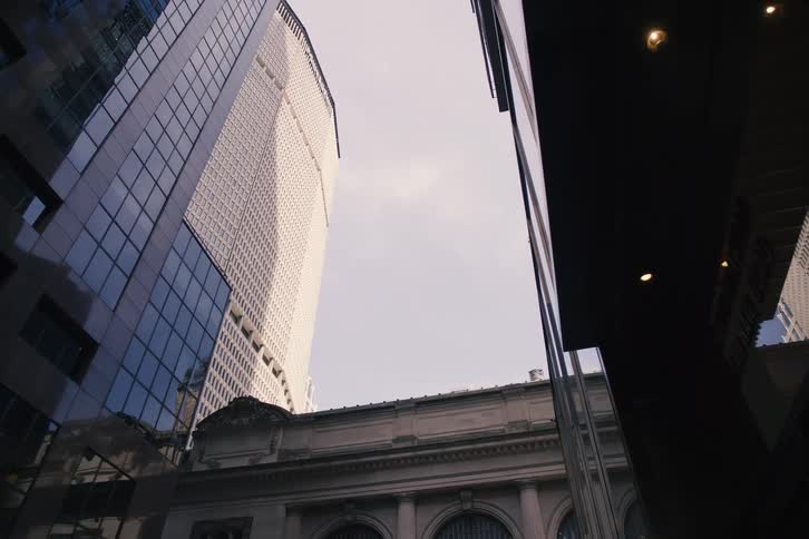 A slow, low-angle reveal of towering skyscrapers with reflective glass facades contrasting with classical architecture