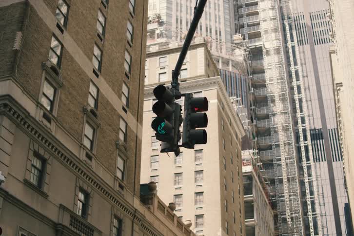 A green pedestrian walk sign on a traffic light hangs between tall city skyscrapers in an urban environment