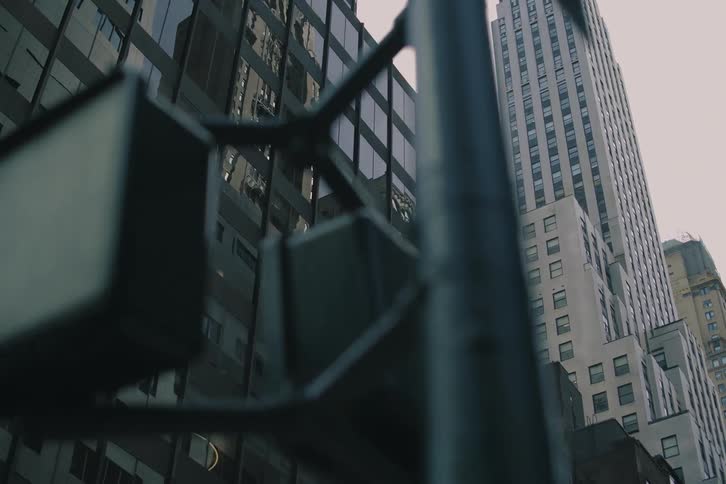 A slow, cinematic camera movement pulls back from a building's reflective windows to reveal a towering city street corner