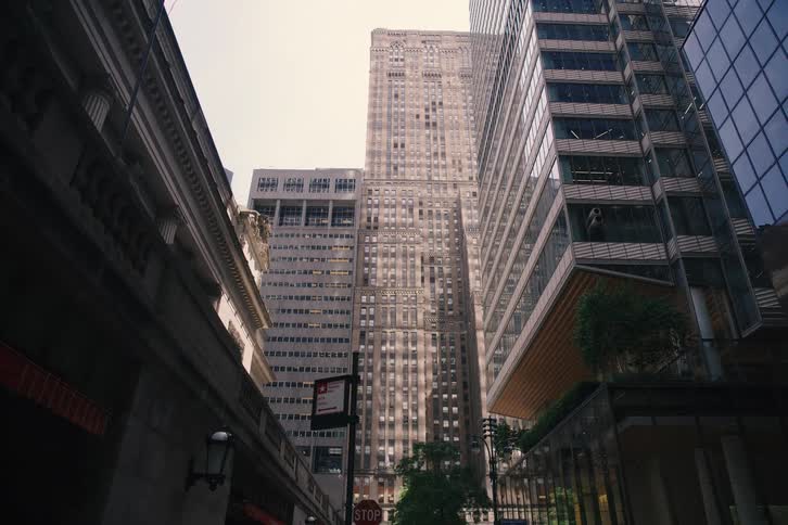 A dramatic slow-motion push-in shot moves along a city street between towering skyscrapers towards a stop sign
