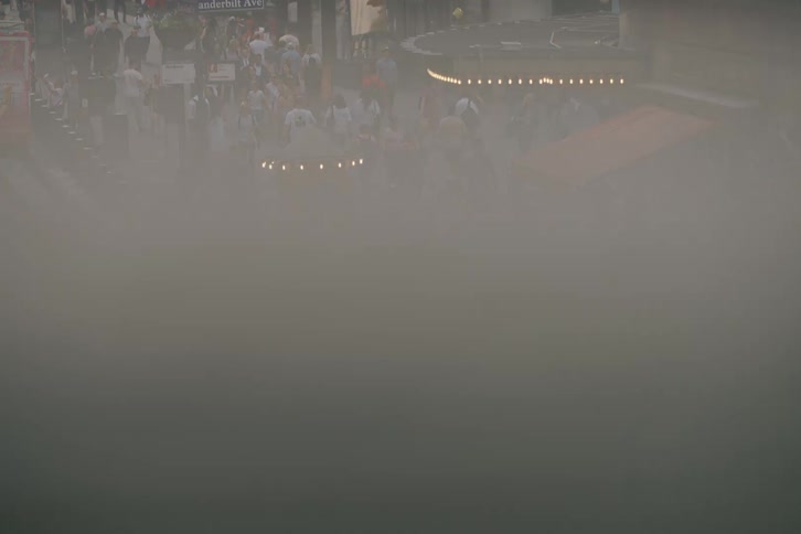 An atmospheric high-angle view of a busy New York City street with crowds of pedestrians, yellow cabs, and haze rising from below
