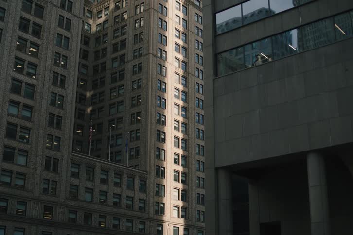 A slow tilt-up reveals the striking contrast between sunlit classic architecture and modern shadowed buildings in a dense city