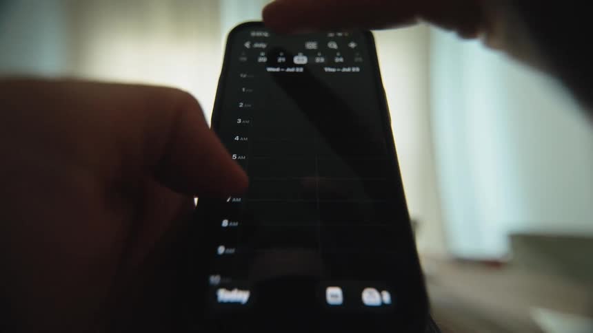 A close-up shot of a person scrolling through and managing their schedule on a digital calendar app on a smartphone in dark mode