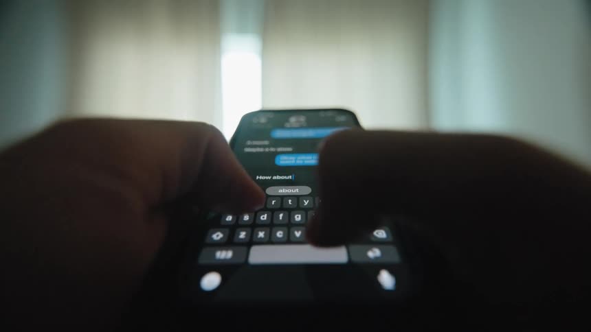 Close-up point-of-view of a person's hands typing and sending messages on a smartphone in a dark room