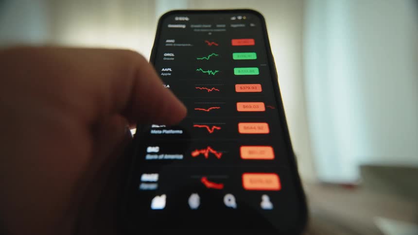 Close-up of a person's hand scrolling through a stock market trading app on a smartphone, analyzing financial charts and data