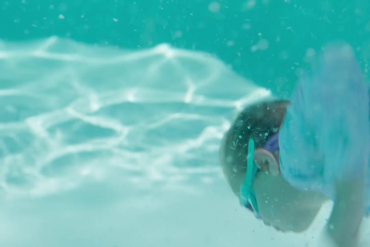 A little girl jumps and dives underwater in a swimming pool to retrieve rings from the bottom in slow motion