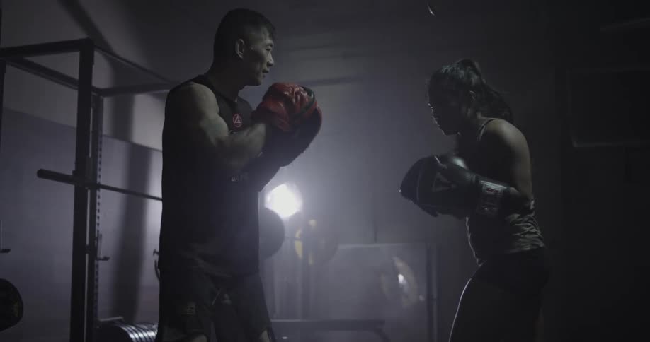 Two people box in a dark gym