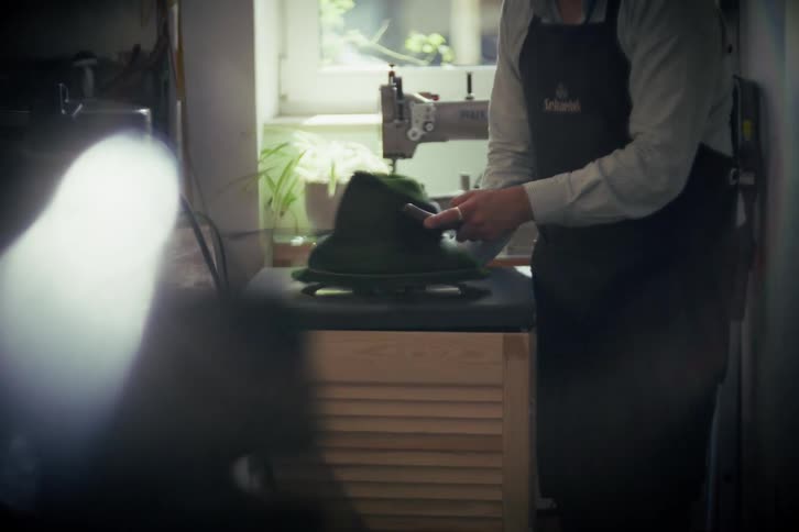 A skilled hat maker meticulously shapes a traditional green felt hat on a spinning machine in his workshop