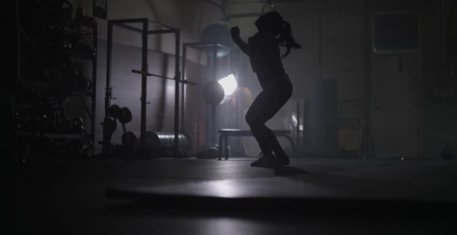 Woman jumps and waves arms in a dimly lit gym