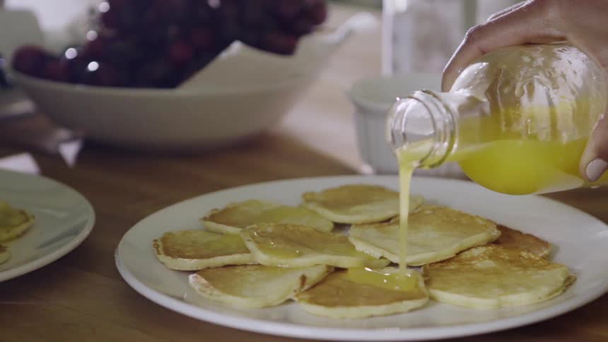 A juice is poured onto pancakes set on a plate