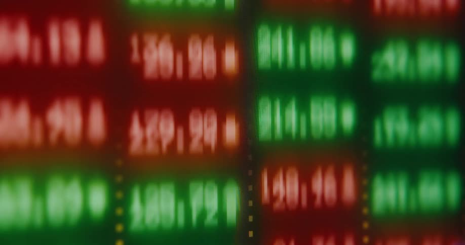 An abstract, out-of-focus digital stock market display shows red and green numbers rapidly fluctuating