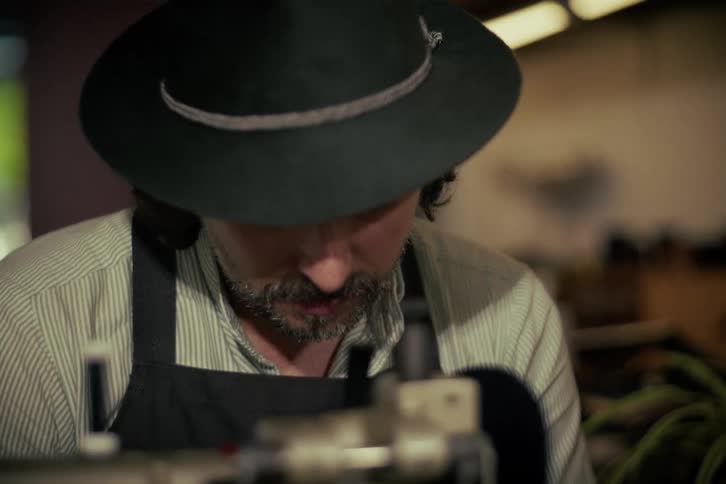 Close-up of a man with a hat and apron focused on his work in a dimly lit workshop
