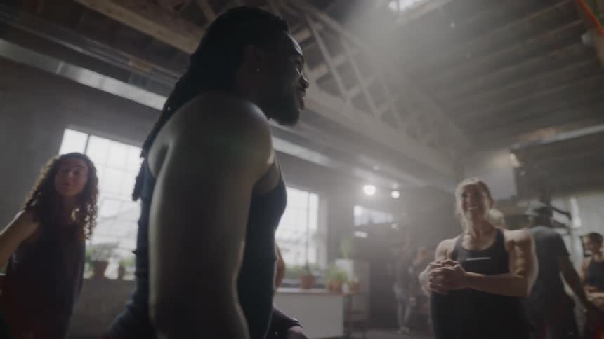 A male fitness instructor with dreadlocks motivates his diverse class in a sunlit gym studio