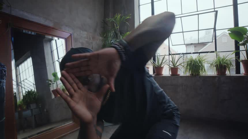 A focused Black man performs an expressive, slow-motion dance in a sunlit industrial loft