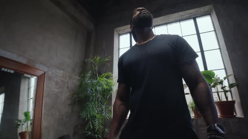 Low angle shot of a muscular man standing in a moody, industrial-style gym, looking up with determination
