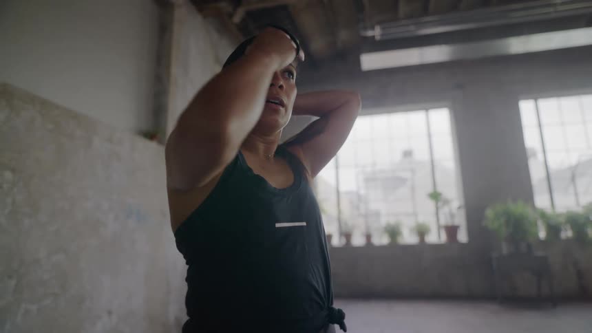 A determined woman ties her hair up in a ponytail in slow motion, focusing before her workout in an industrial gym