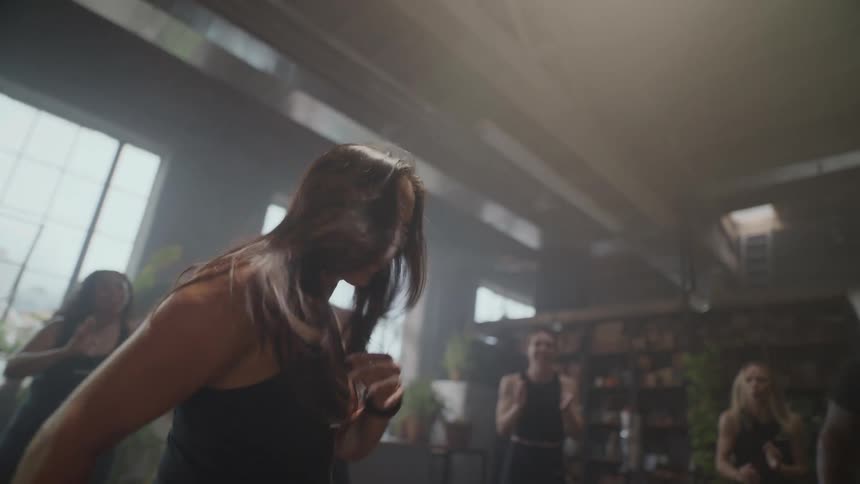A determined woman runs with intensity during a slow-motion group fitness class in a sunlit studio